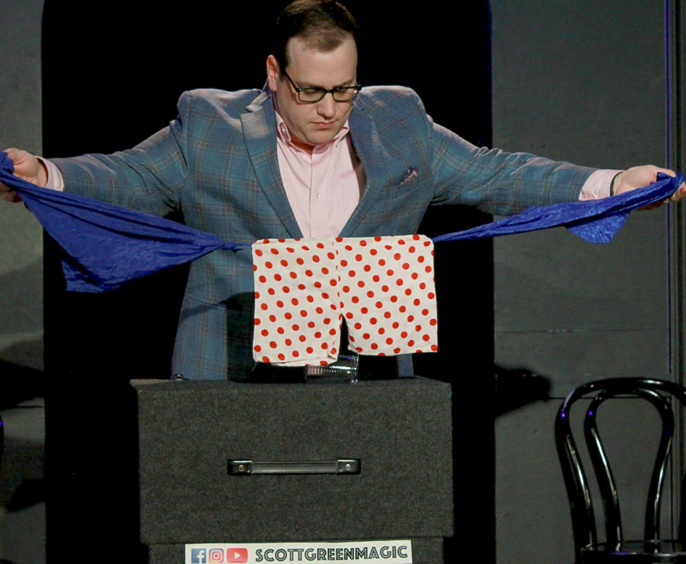 Scott Green pulling a blue silk away to reveal polka-dot boxer shorts on stage at iO Theater
